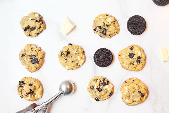 Cookies laid out with cookie scoop white chocolate and oreos on white marble.