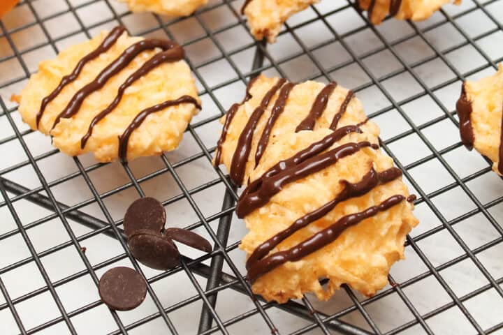 Chocolate drizzled orange macaroons on wire rack with chocolate chips.