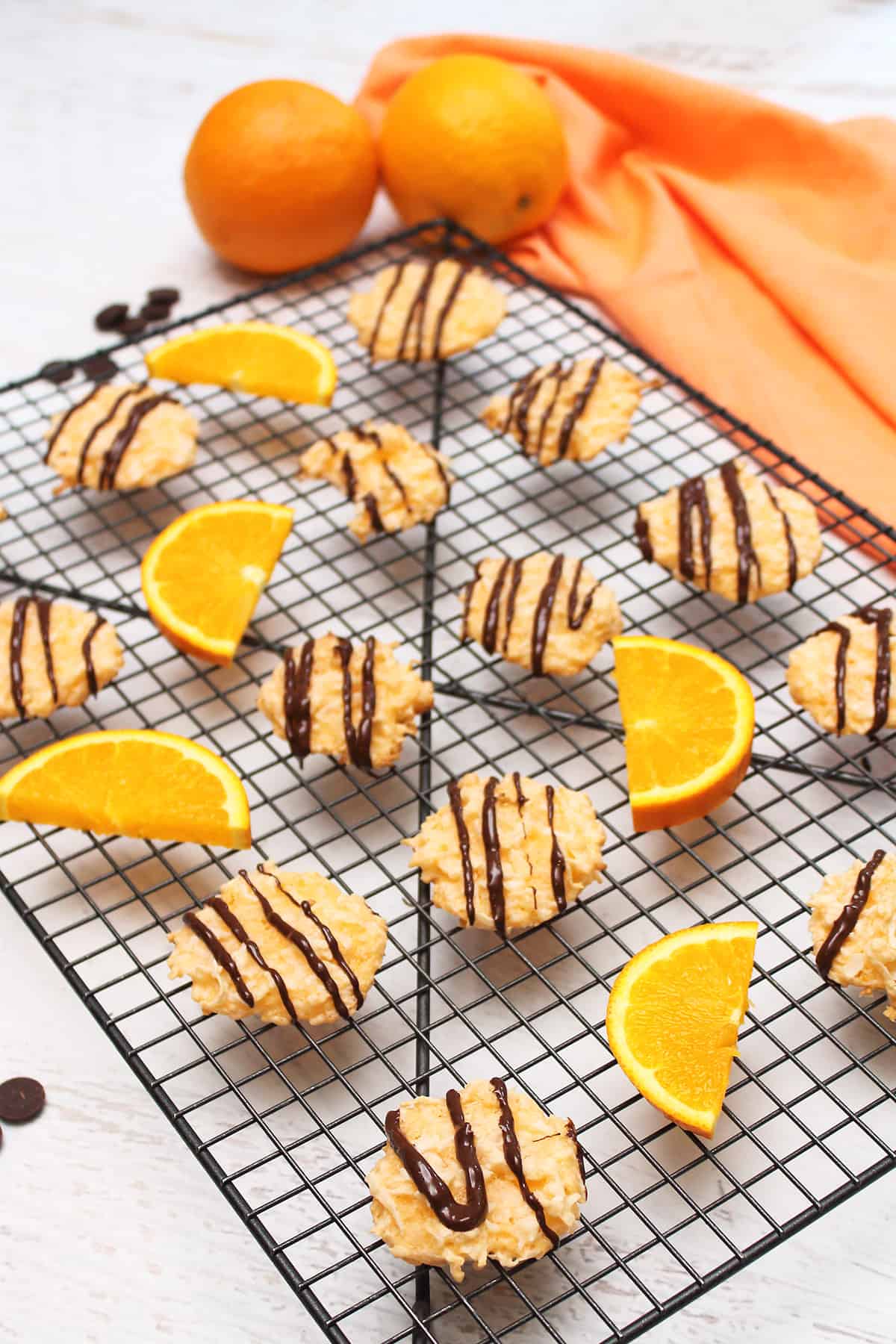 Orange Macaroons drizzled with chocolate on wire rack with oranges around them.