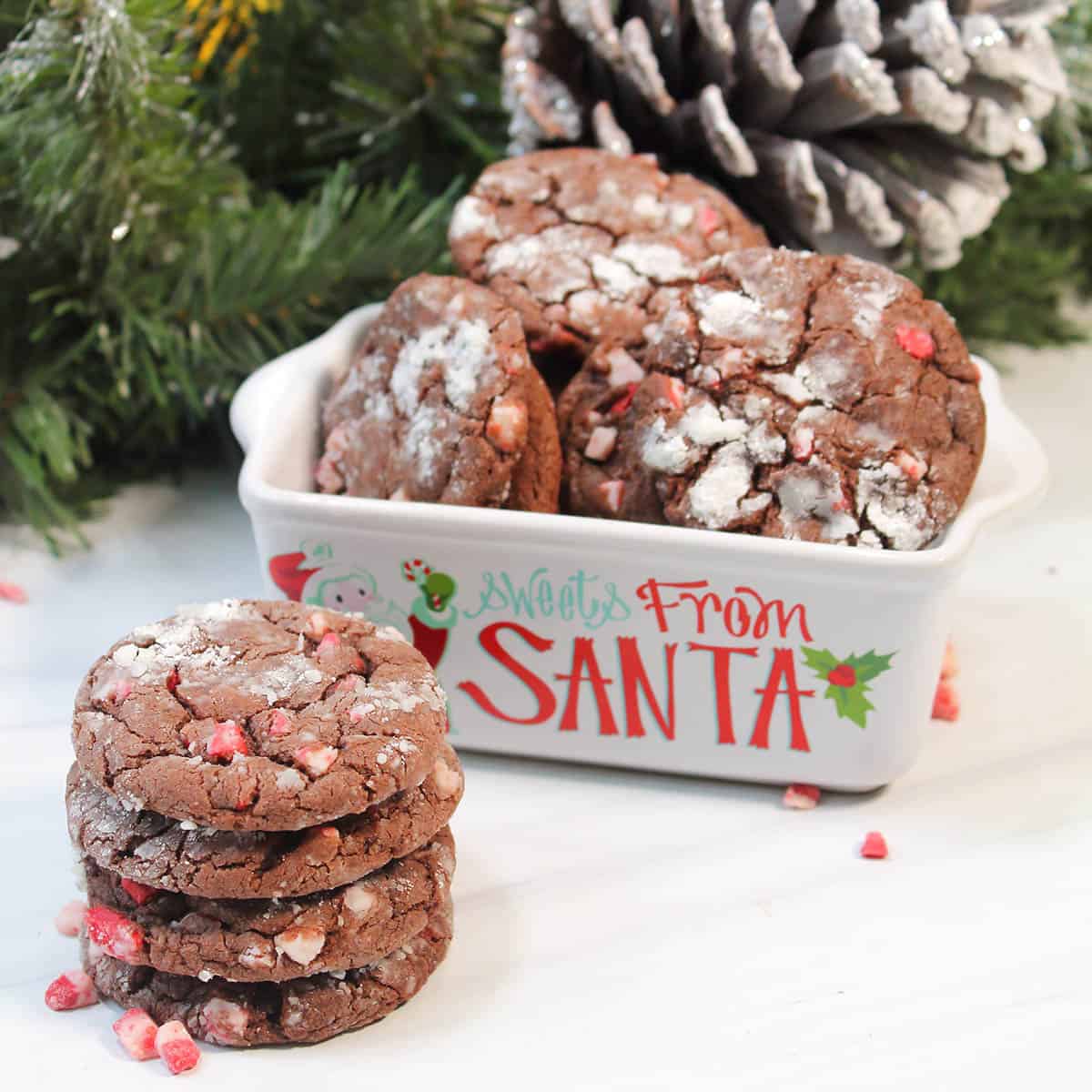 Stack of chocolate cake mix cookies with peppermint in front of Christmas dish.