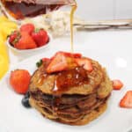 Drizzling syrup over stack of pancakes with sliced strawberries..