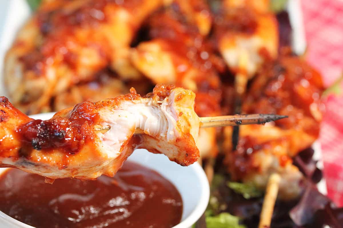 Holding grilled chicken skewer with bite out of it.