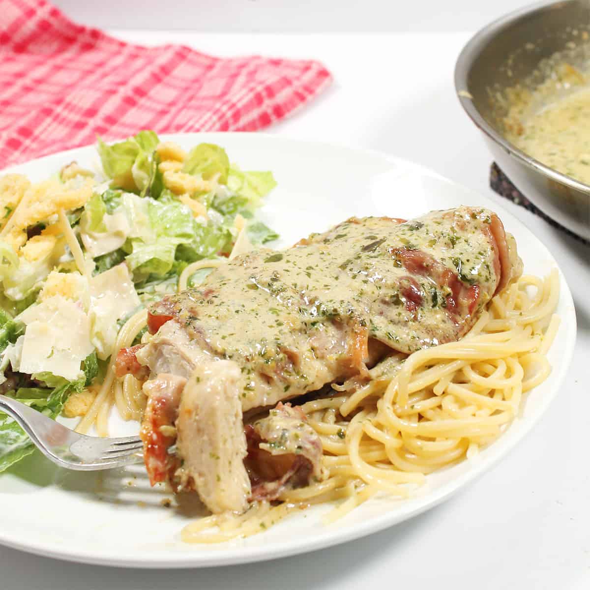 Bite of prosciutto chicken on fork beside salad.