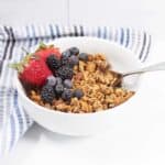Honey granola in a bowl with fruit and a spoon.
