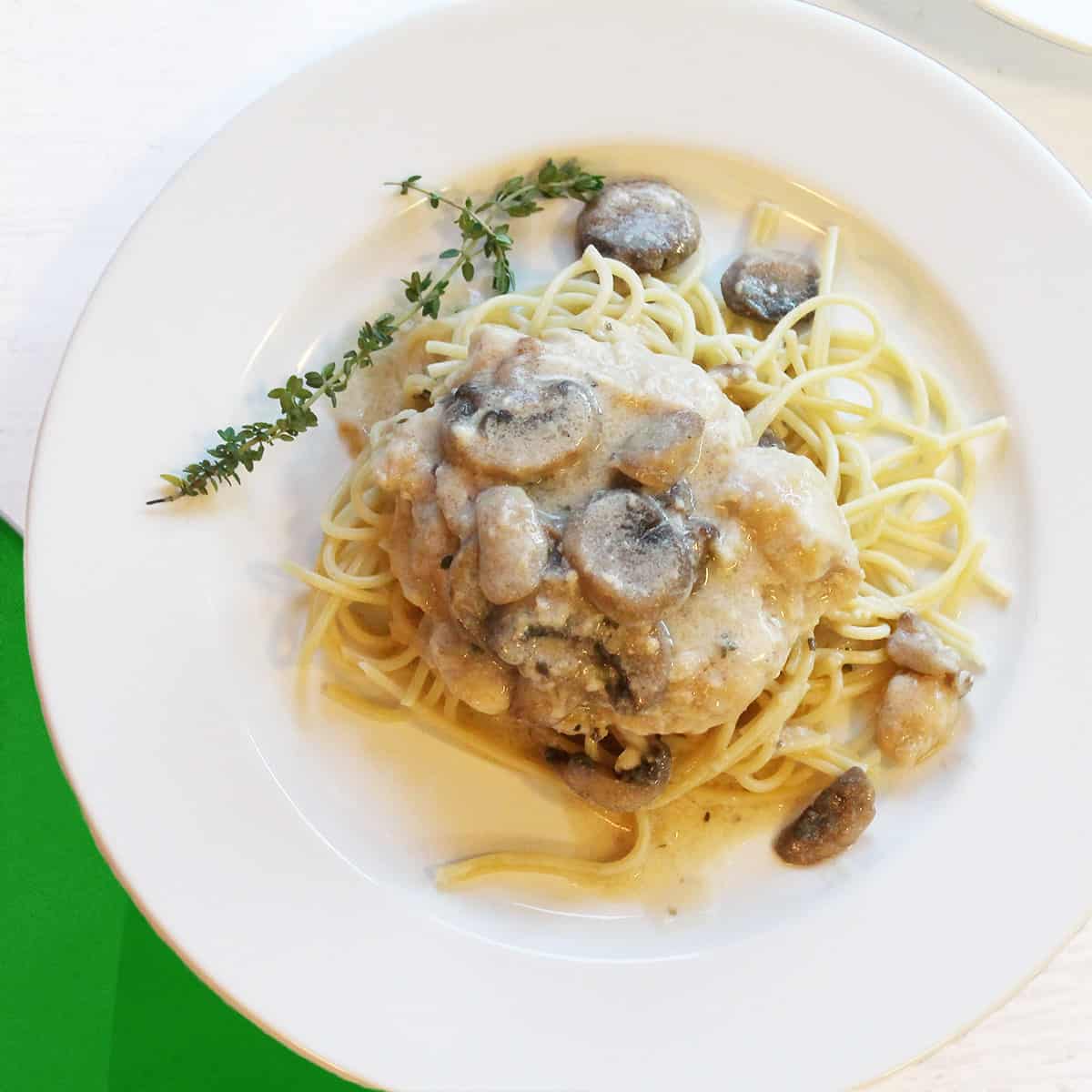 Overhead of white wine sauce with asiago cheese over chicken.