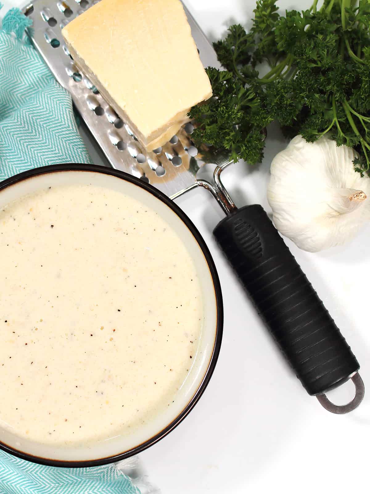 Partial view of bowl with asiago sauce with cheese and garlic.