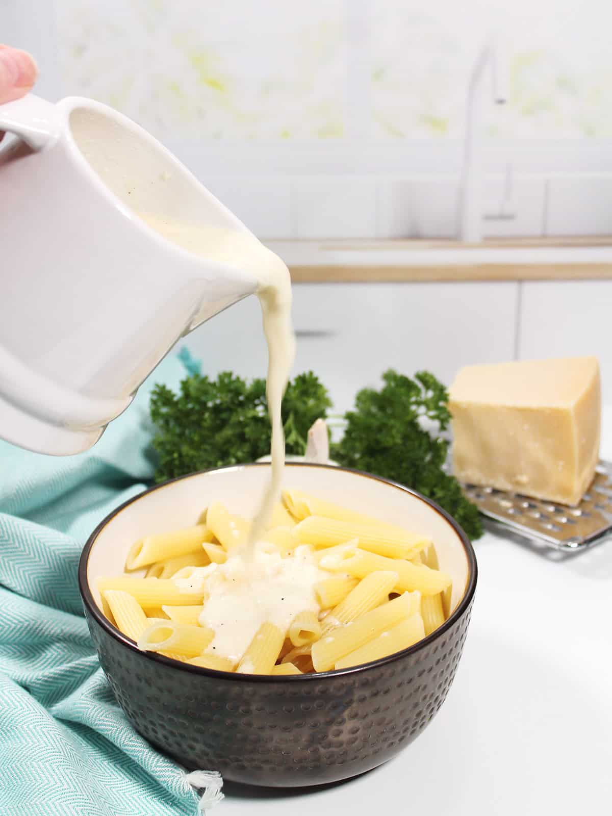 Pouring asiago cream sauce over pasta.