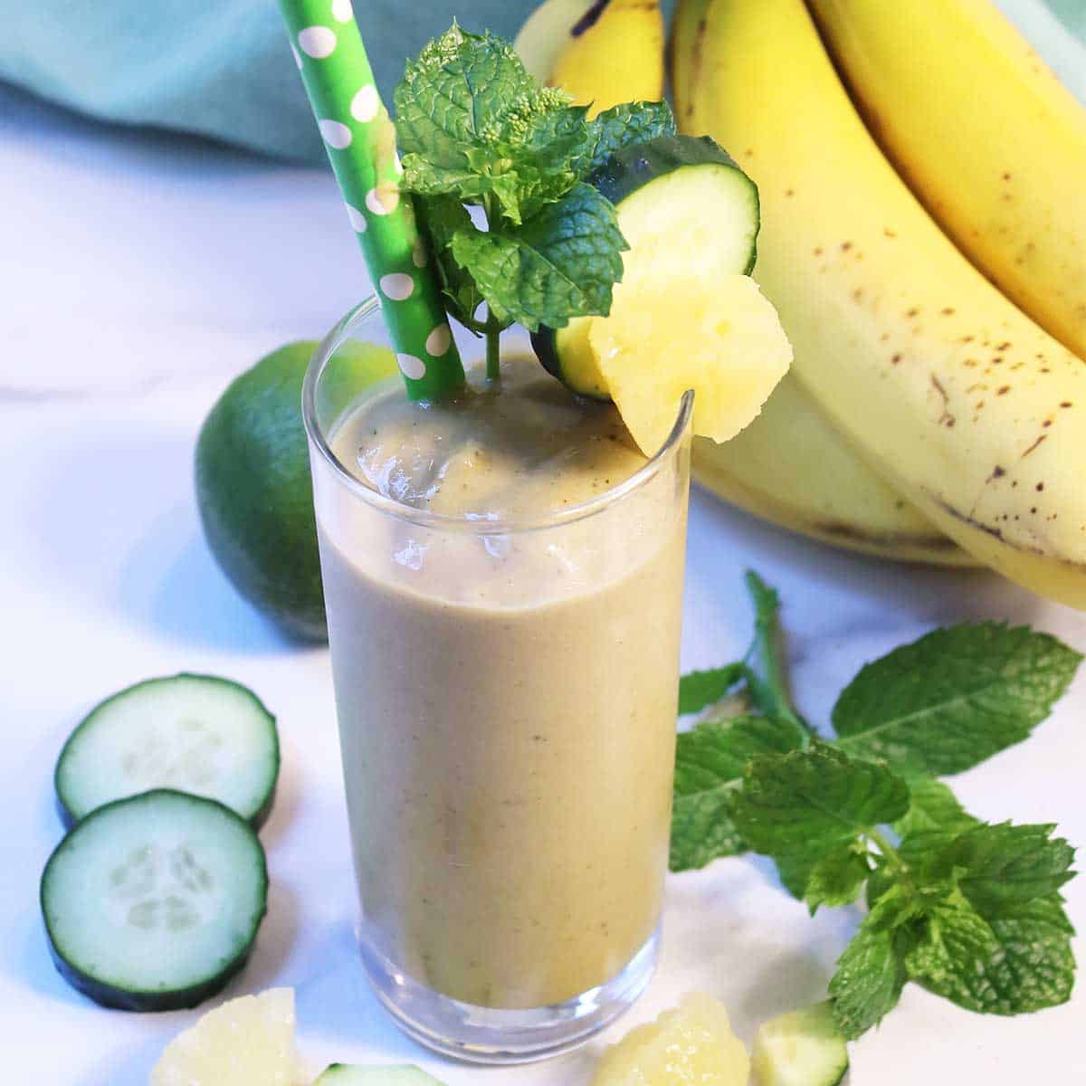 Garnished pineapple and banana smoothie with fruit and mint around base.