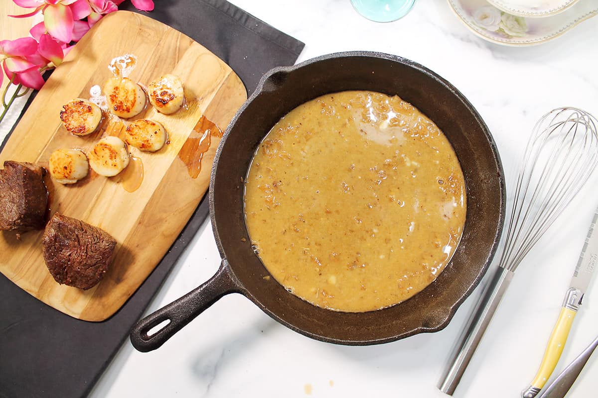 Butter sauce in skillet next to seared steak and scallops.