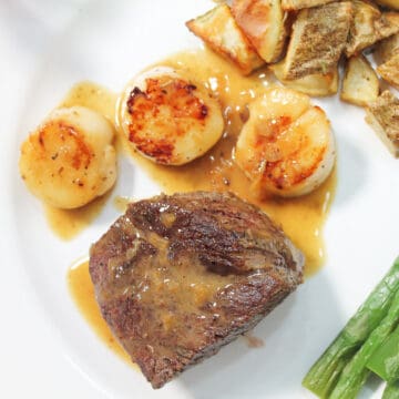Overhead closeup of champagne butter sauce drizzled over filet mignon and scallops.