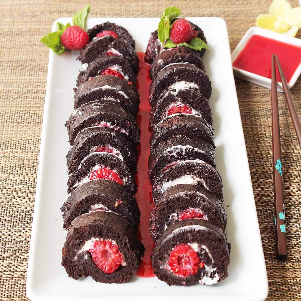 Two raspberry sushi rolls on white platter with raspberry sauce.