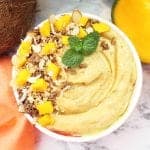 Closeup of smoothie in white flowered bowl with garnishes of coconut mango and granola.