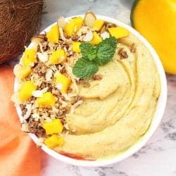 Closeup of smoothie in white flowered bowl with garnishes of coconut mango and granola.