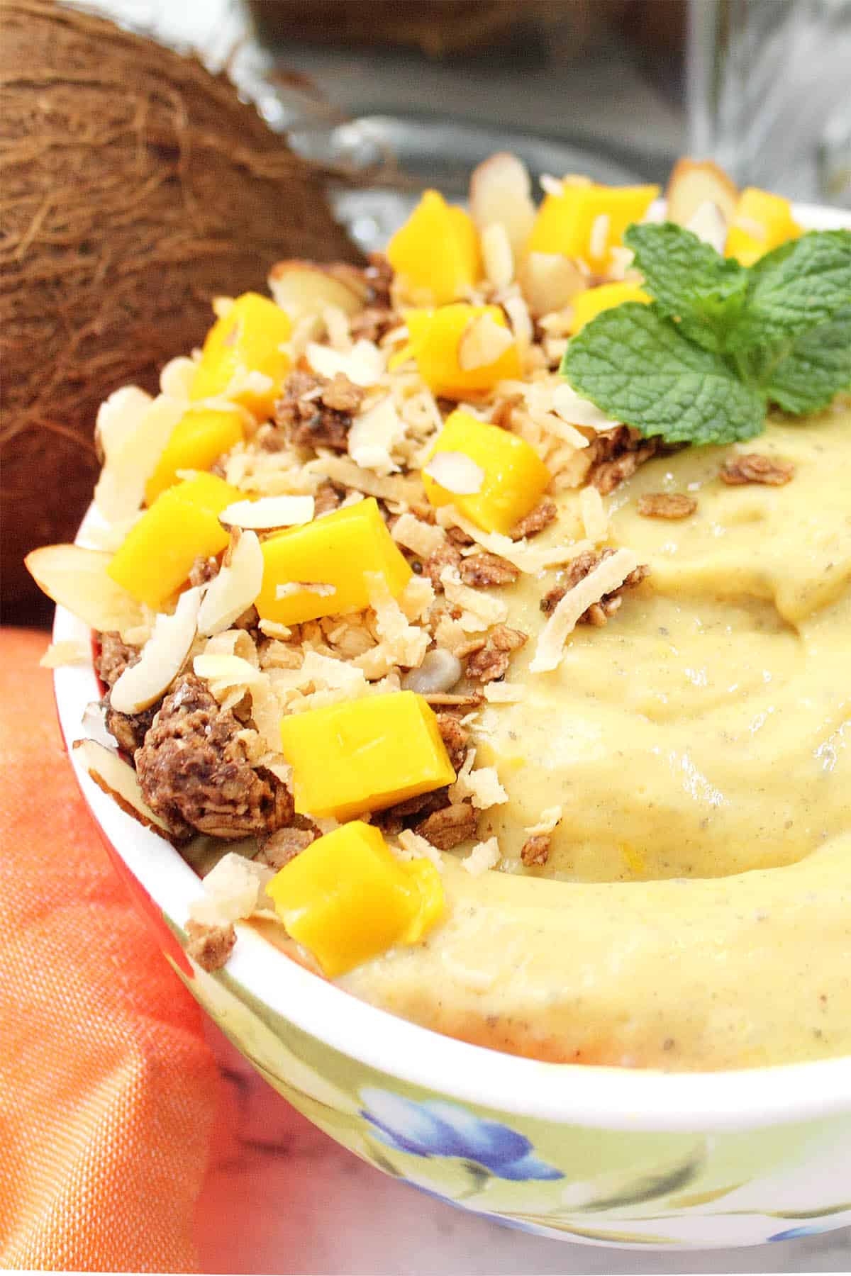 Partial side view of mango smoothie bowl garnished with coconut granola and diced mango.