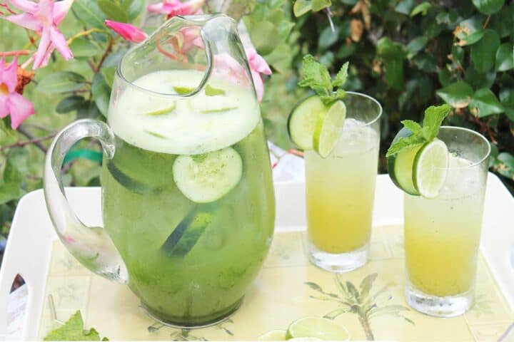 Pitcher and two filled glasses on palm tree tray.
