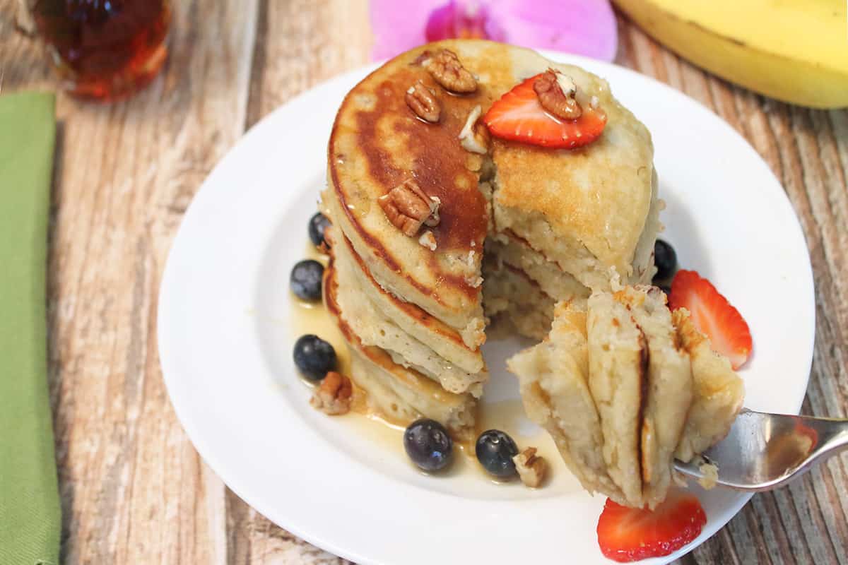 Forkful of almond flour banana pancakes on plate by stack of pancakes.
