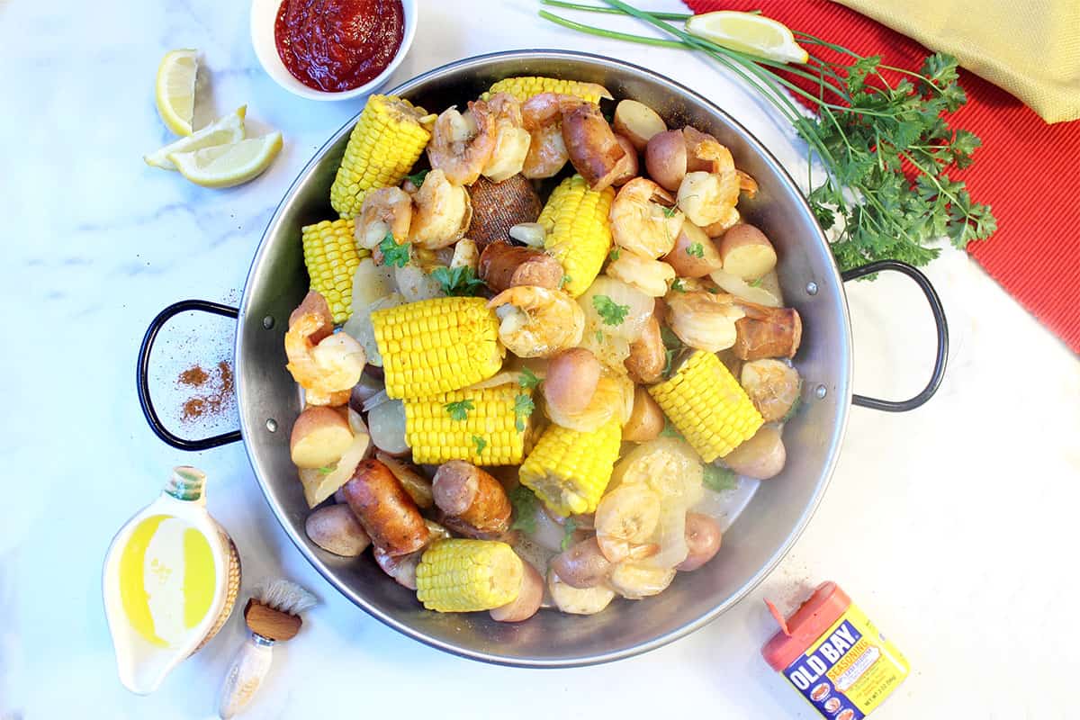 Overhead of hot shrimp boil in round pan with old bay cocktail sauce and butter.