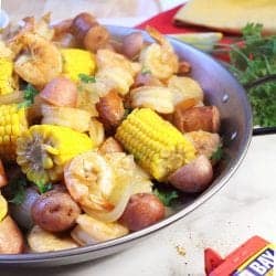 Partial view of low country boil in round pan with parsley and red and gold napkin in corner.
