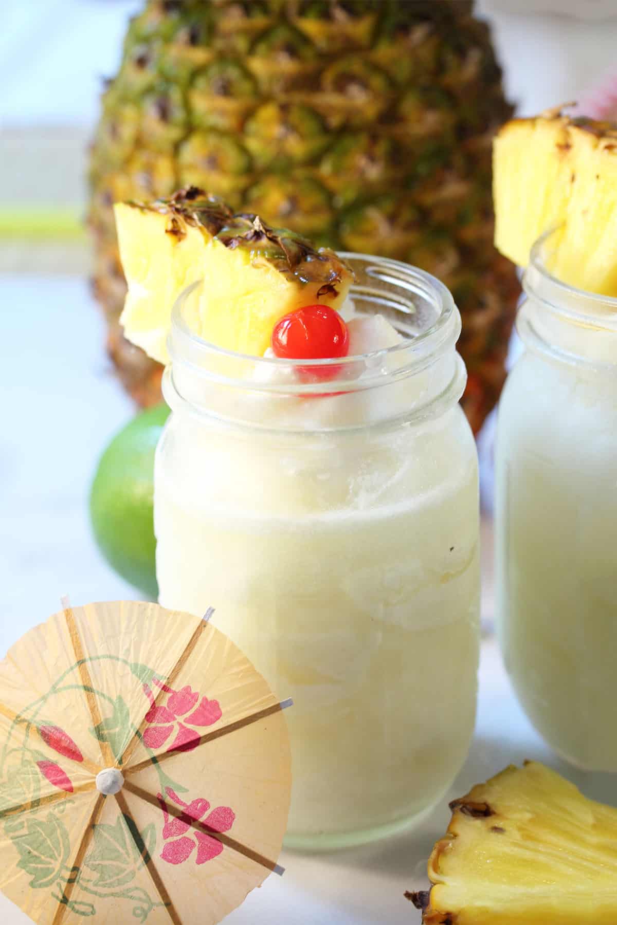 Pina colada in mason jar with pineapple and cherry garnish.