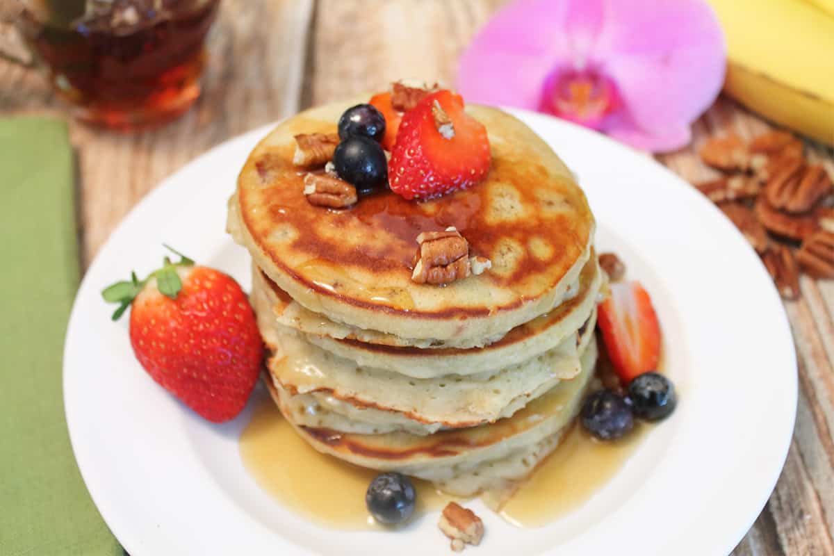 Stack of healthy pancakes on white plate with fruit and nut topping.
