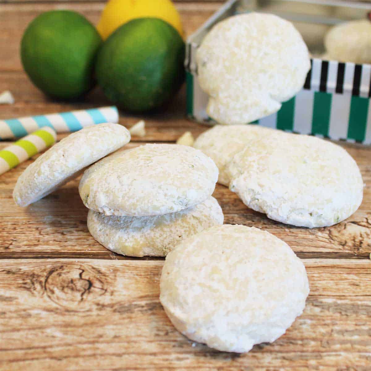 Closeup of cookies on wooden table with cookie tin and limes.