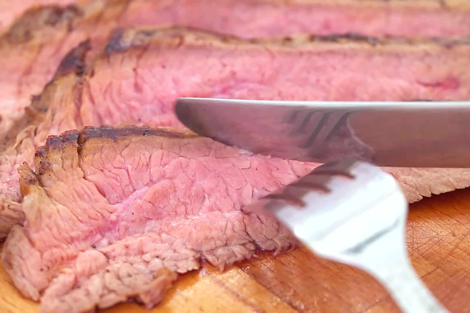 Cutting a bite of medium rare london broil.