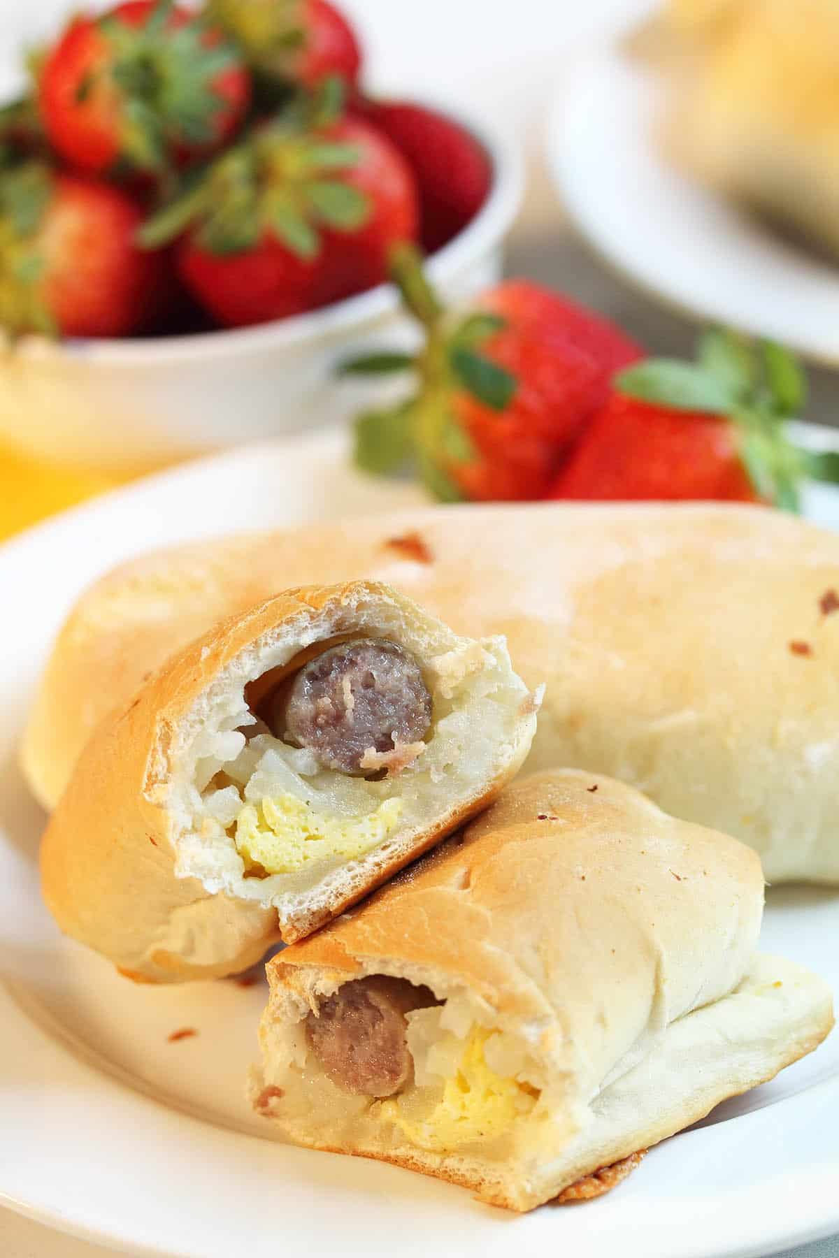 Kolaches cut in half on white plate with strawberries in background.