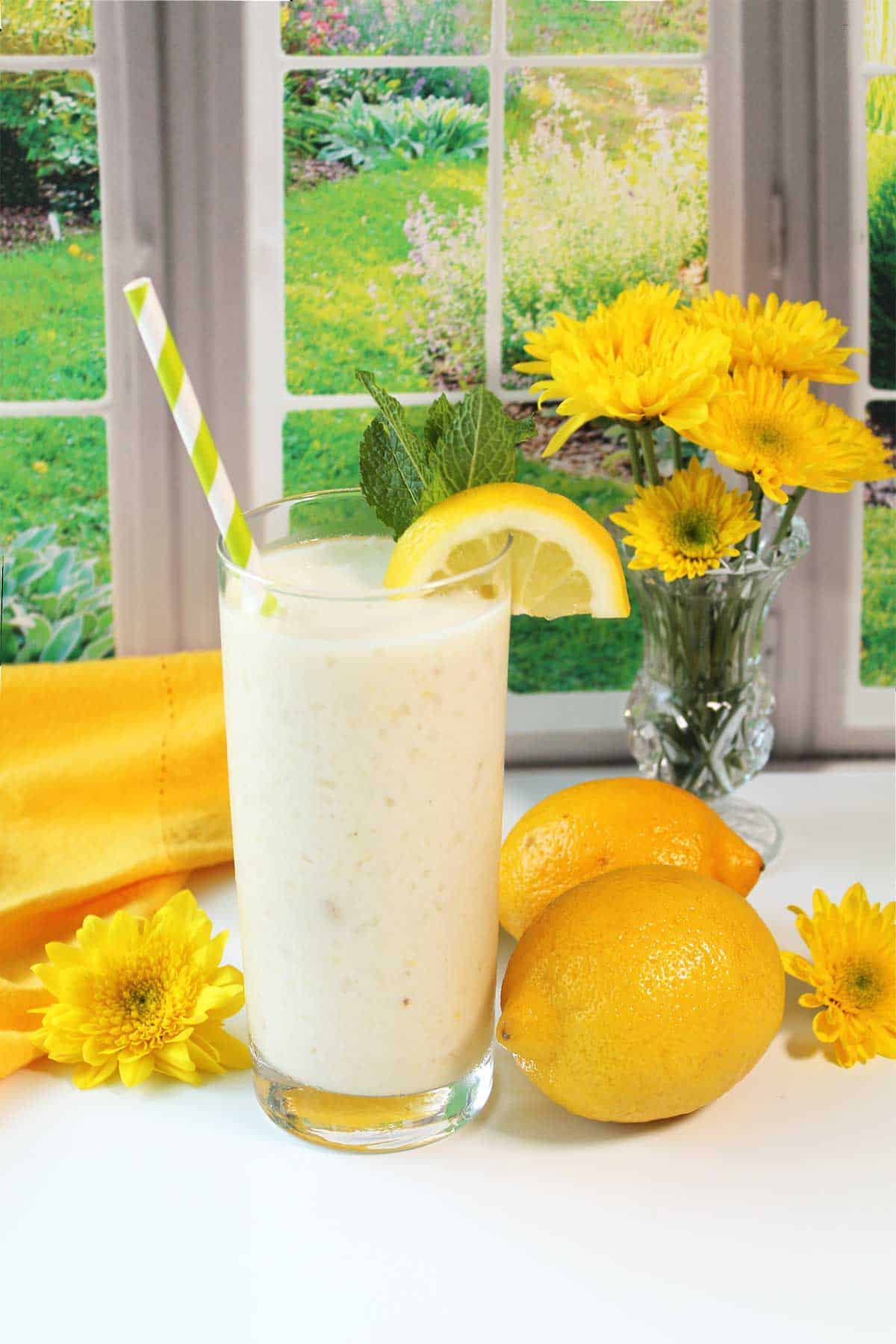 Lemon Smoothie with lemon garnish and straw by window.