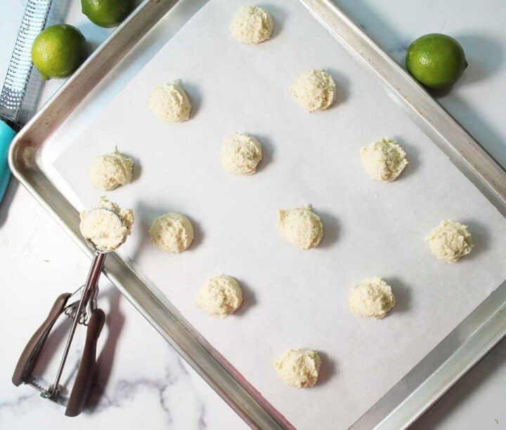Scoops of lime cookies on a cookie sheet with scooper, zester and limes around it.