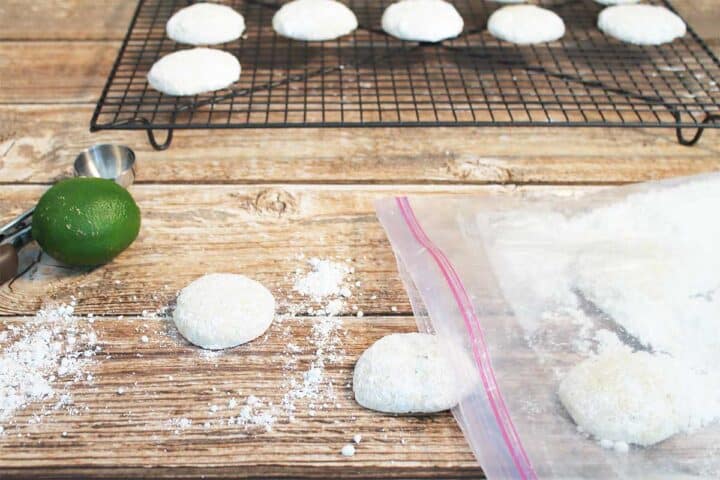 Sugar coated cookies on wooden table next to bag of powdered sugar.
