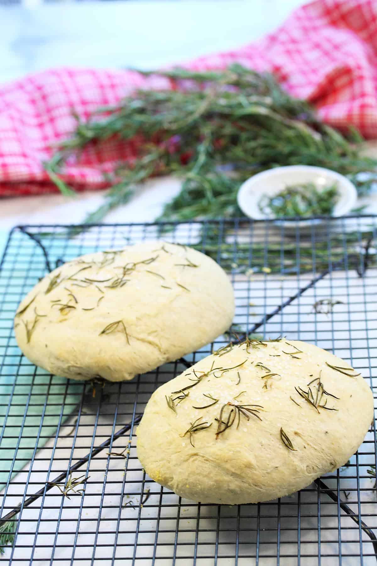 Freshly baked breads cooling on rack in front of rosemary.