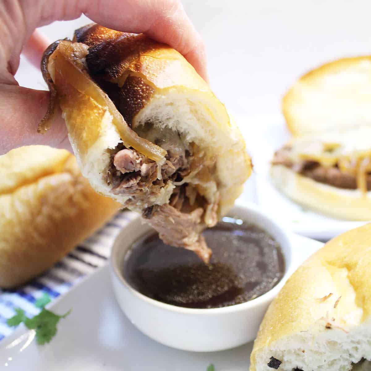 Dipping french dip sandwich into au jus.