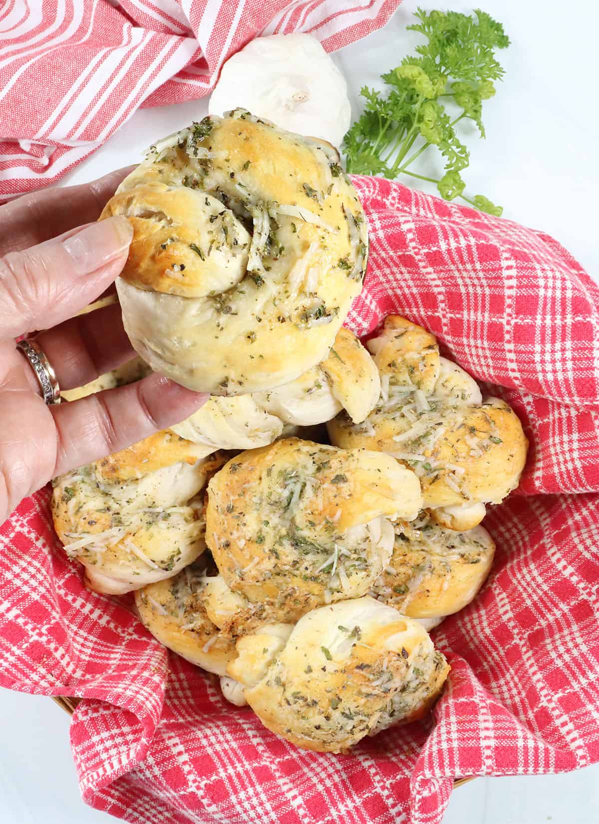 Holding a garlic parmesan knot over a basket of garlic knots made with biscuits.