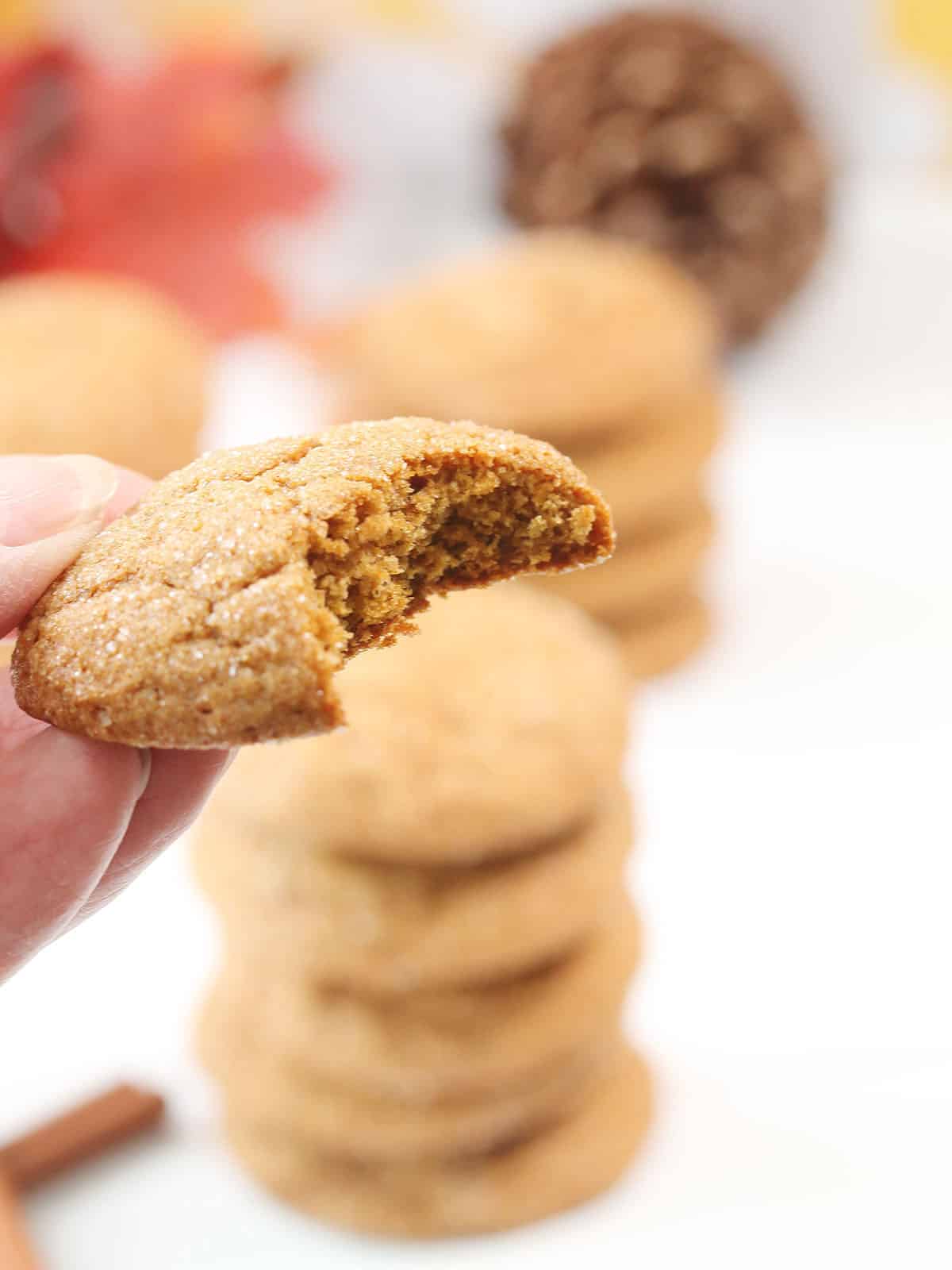 Holding pumpkin pie spice cookie with bite out.