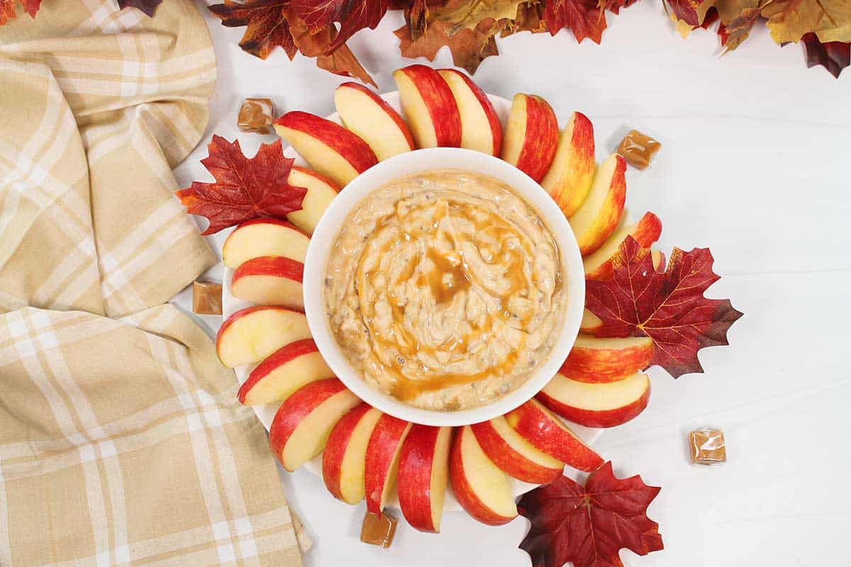 Caramel apple dip with cream cheese surrounded by apples and ready to serve.