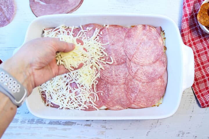 Sprinkling shredded mozzarella on top of salami.