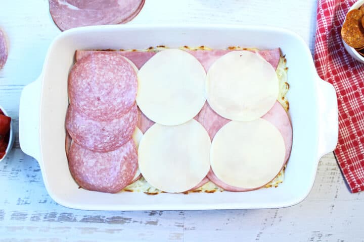 Adding layers of provolone cheese slices and salami.