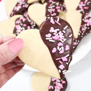 Holding a chocolate dipped sugar cookie decorated for Valentine's Day.