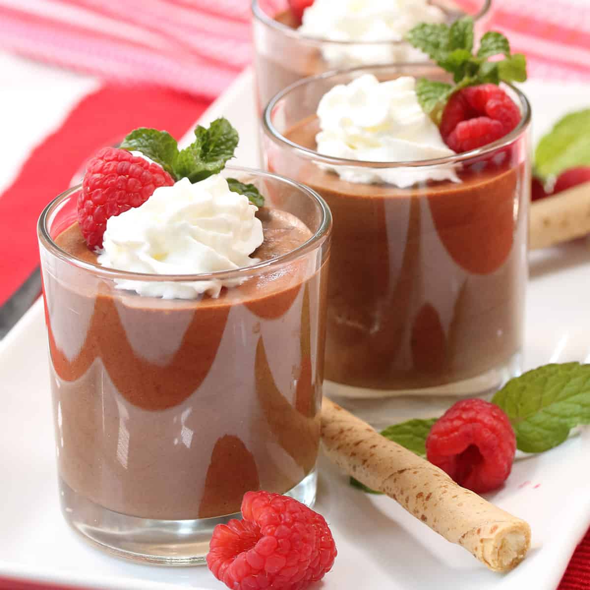 Three garnished servings of coffee mousse on white plate with raspberries and pirouette cookies.