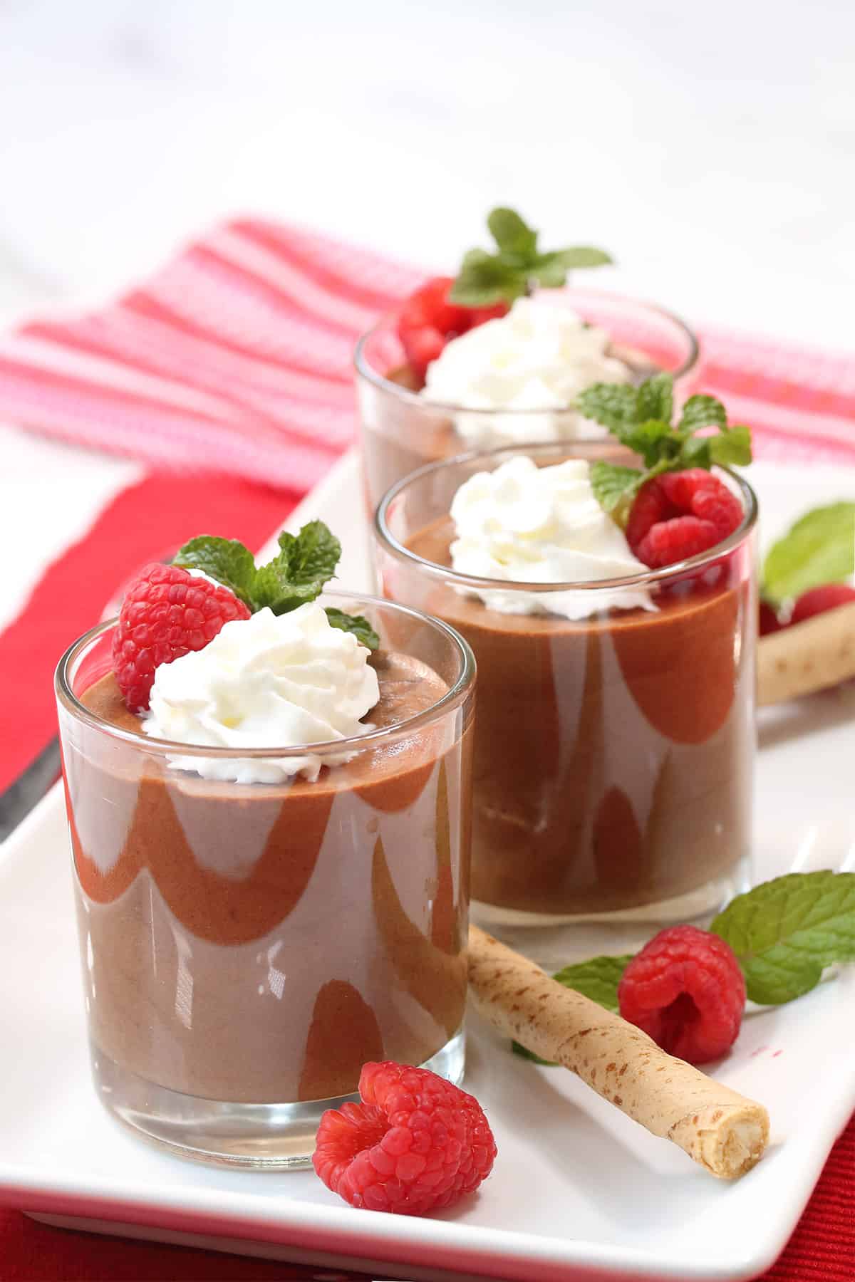 Front view of three servings of chocolate coffee mousse on white platter with raspberries and mint leaves.