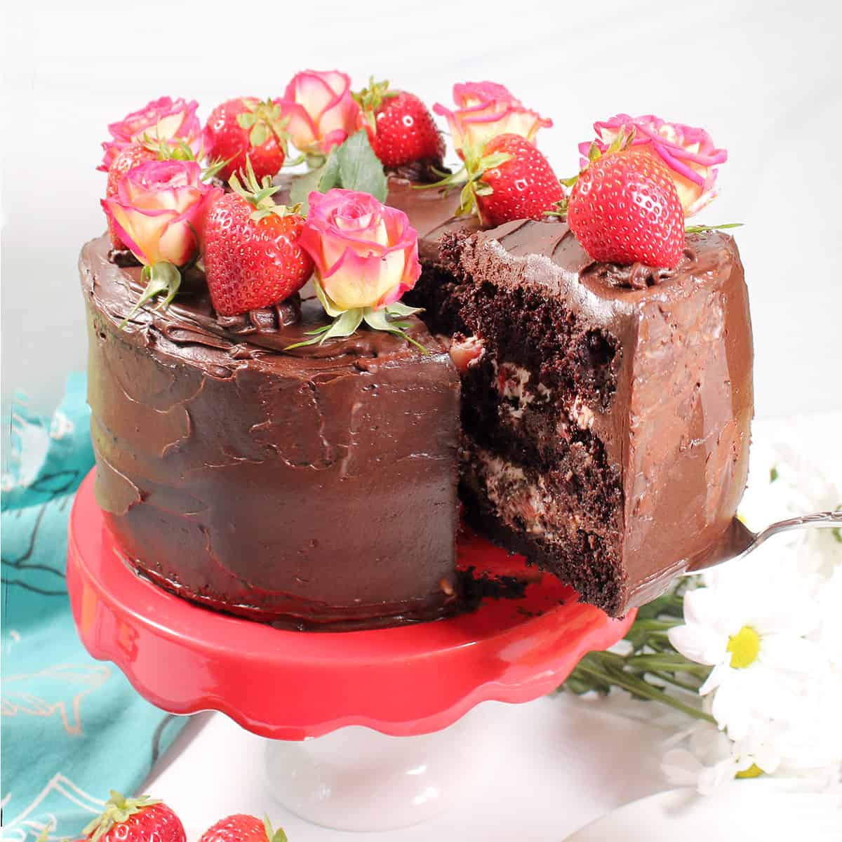 Lifting slice of chocolate cake with strawberries out of full cake.