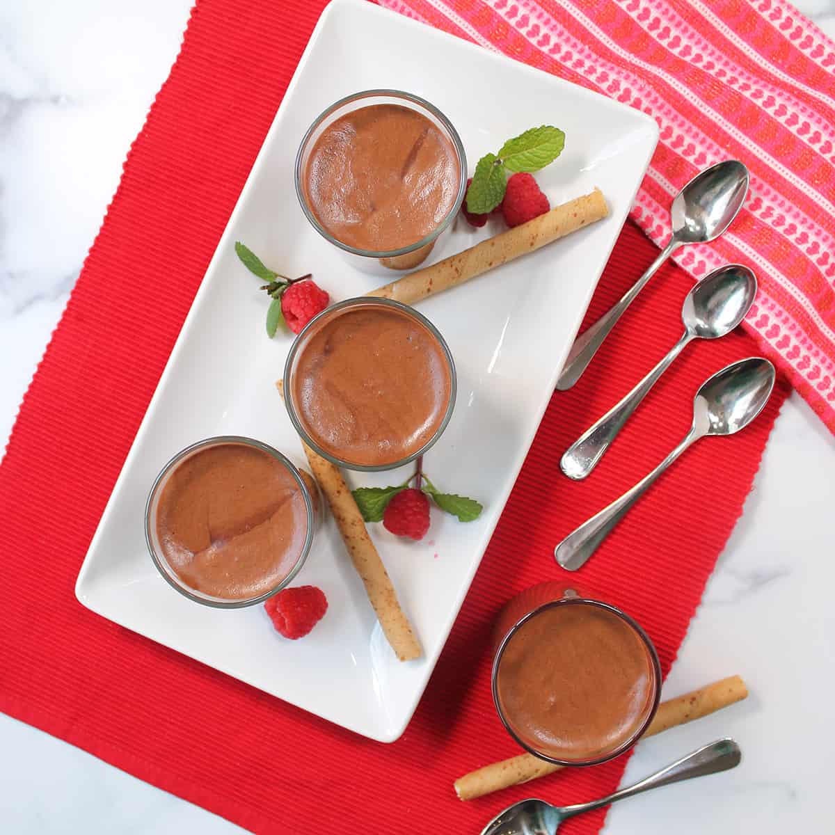 Overhead of ungarnished chocolate mousse on red placemat with spoons.