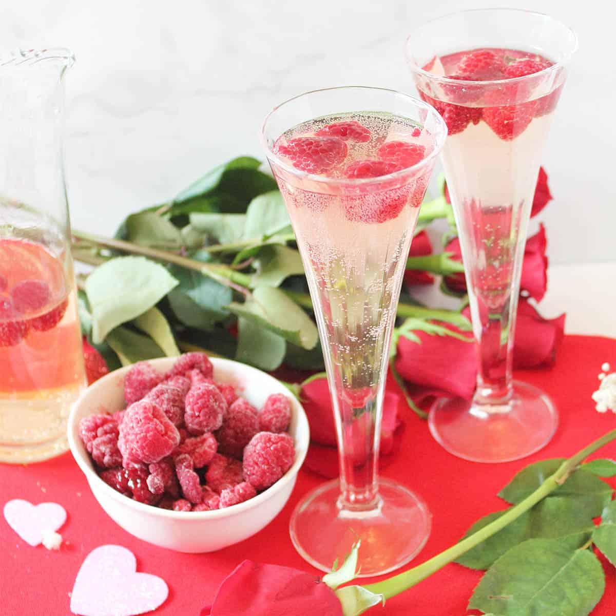 Two glasses of spritzer on red Valentine heart with rose and raspberries.