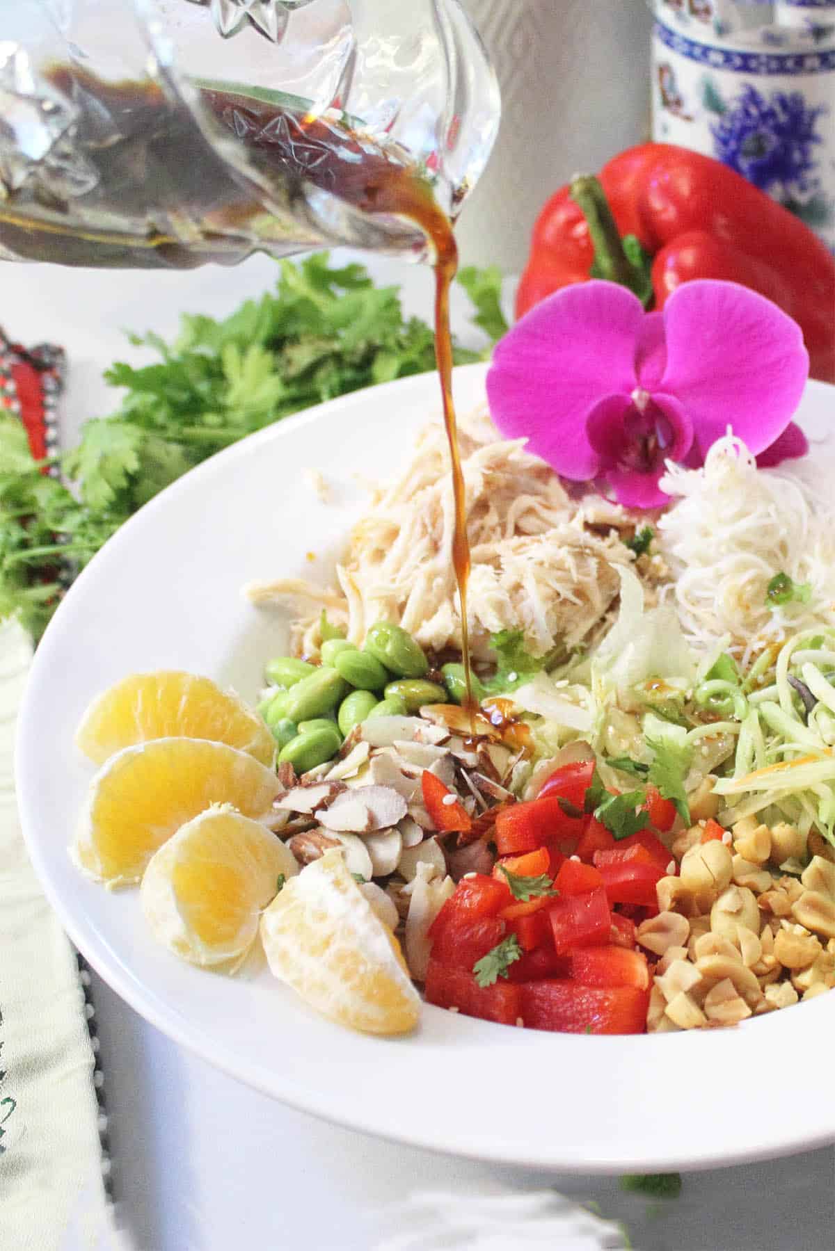 Drizzling dressing on salad in white bowl.