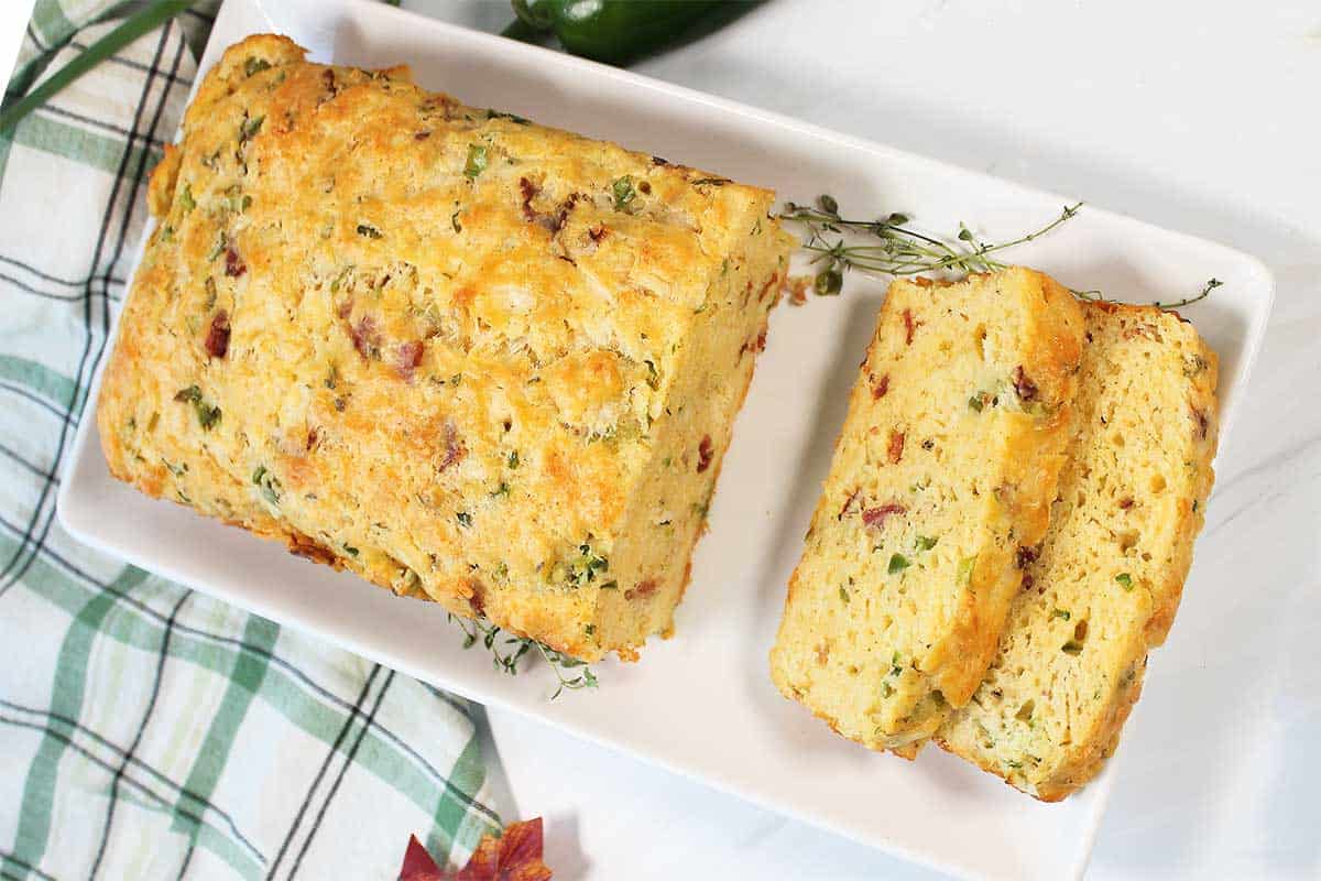 Overhead of slice bacon cheese bread on white platter.