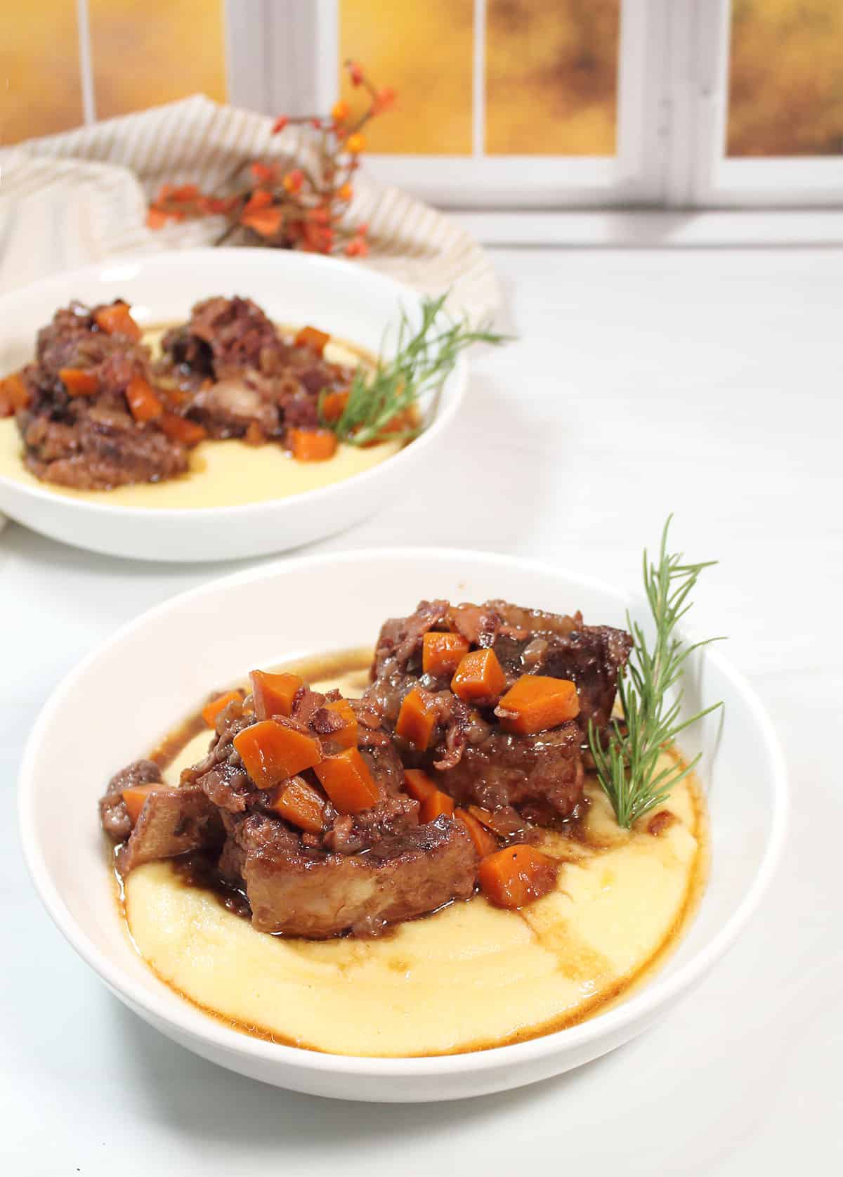 Two plated braised short ribs dinners over polenta with rosemary garnish.