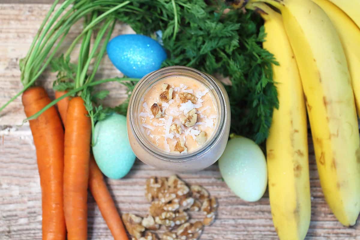 Overhead of carrot smoothie in mason jar with fruits and veggies.