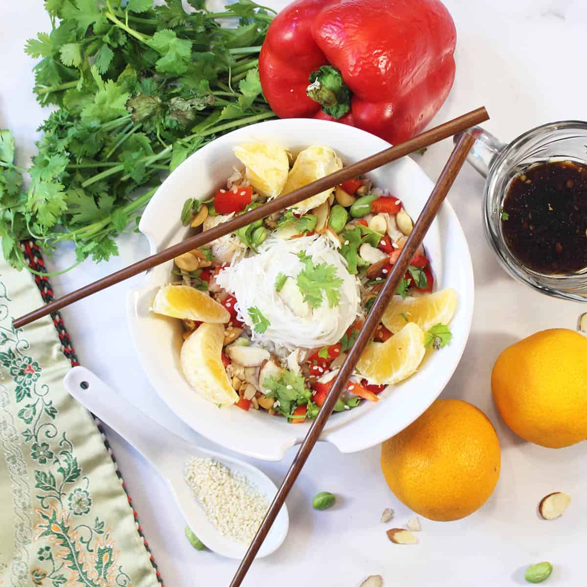 Overhead of noodle bowl with oranges pepper cilantro and scattered almond around it.