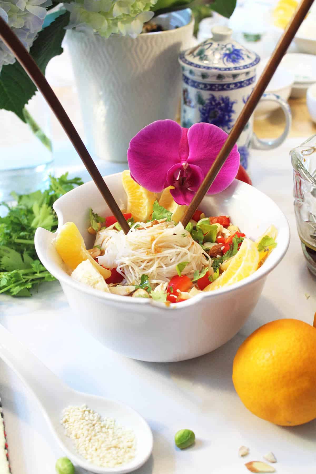 Ready to eat salad on white table with flowers in vase in background.