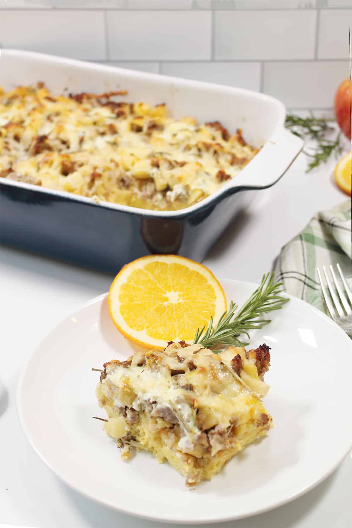 Slice of sausage apple breakfast casserole on plate by casserole.